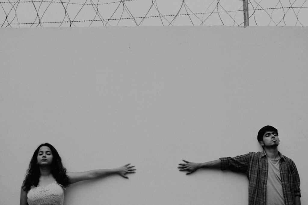 Grayscale Photo of Man and Woman With Arms Extended on Wall