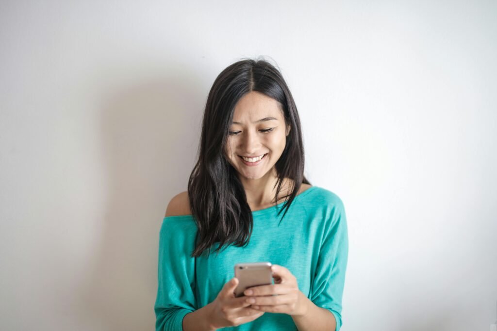 pexels-photo-3756682-3756682 A happy woman in a green top smiling while using her smartphone indoors.
