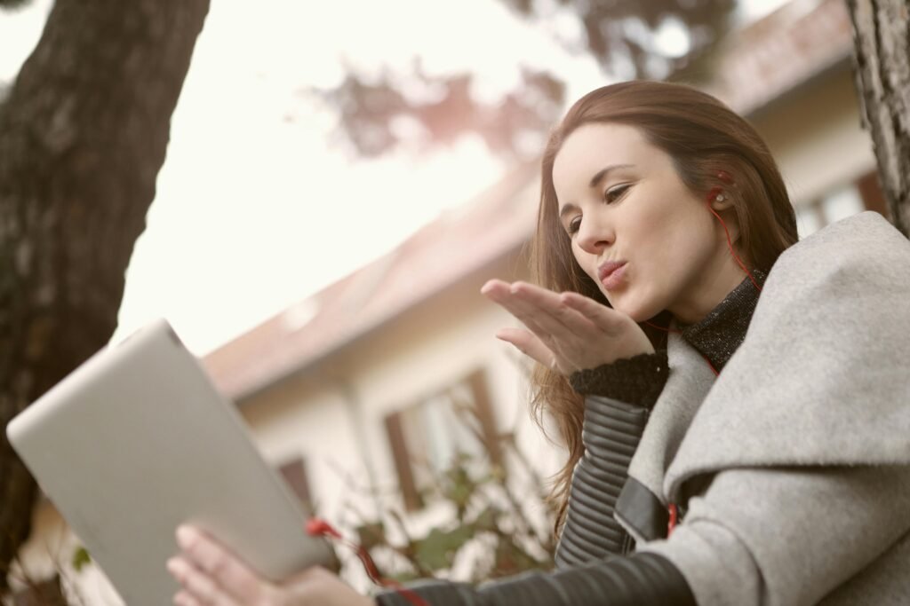 pexels-photo-3783118-3783118 Young woman using a tablet for a video call outdoors, sending a flying kiss.